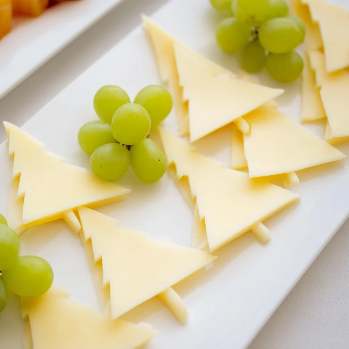 Visually stunning Tannenbaum Border cheese board featuring triangular cheese “trees” and vibrant green grapes.