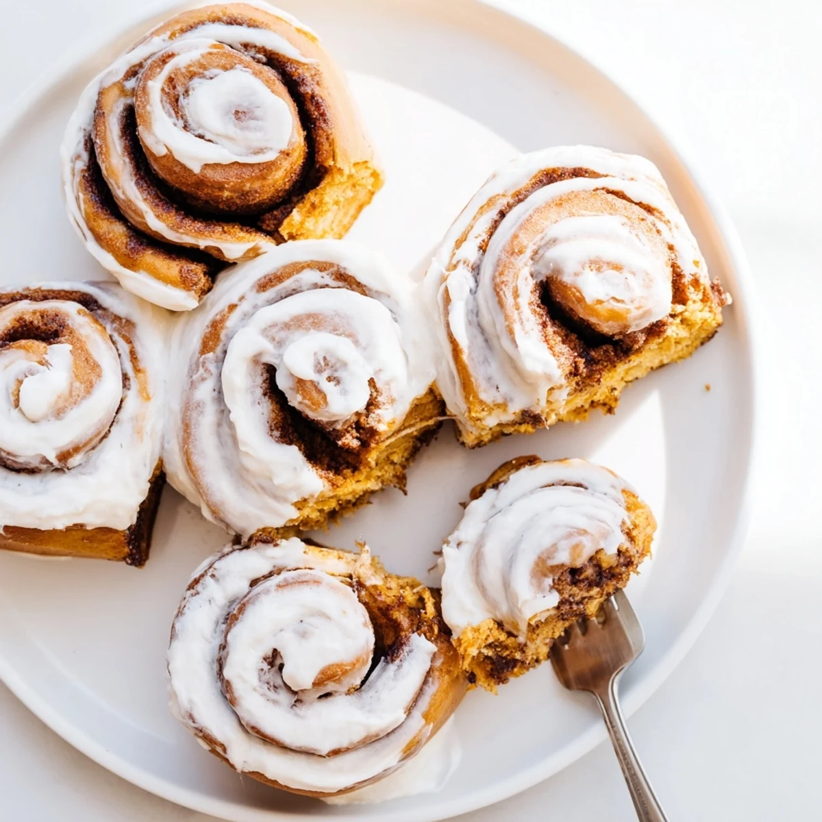 Freshly baked Pumpkin Cinnamon Rolls with golden edges sit in a baking dish, drizzled with creamy frosting.  