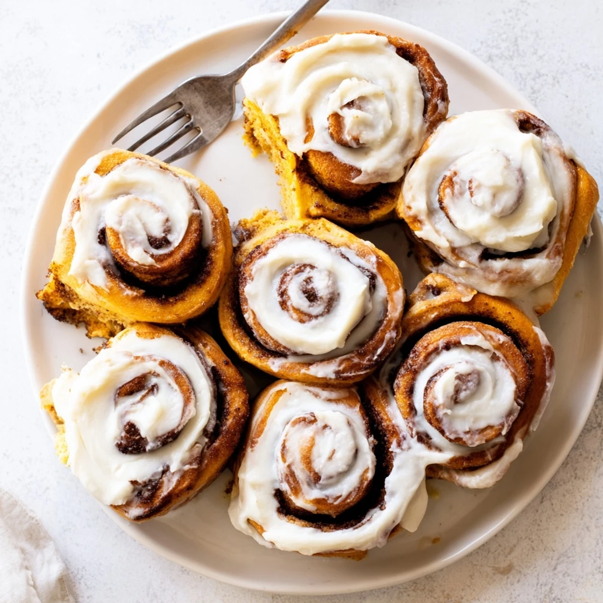 A close-up of a warm Pumpkin Cinnamon Roll reveals its soft, swirled interior and a generous layer of frosting.  