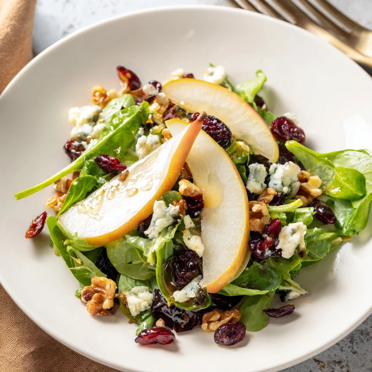 A close-up of a vibrant Pear Gorgonzola Salad featuring crisp mixed greens, juicy sliced pears, and crumbles of tangy blue cheese. 