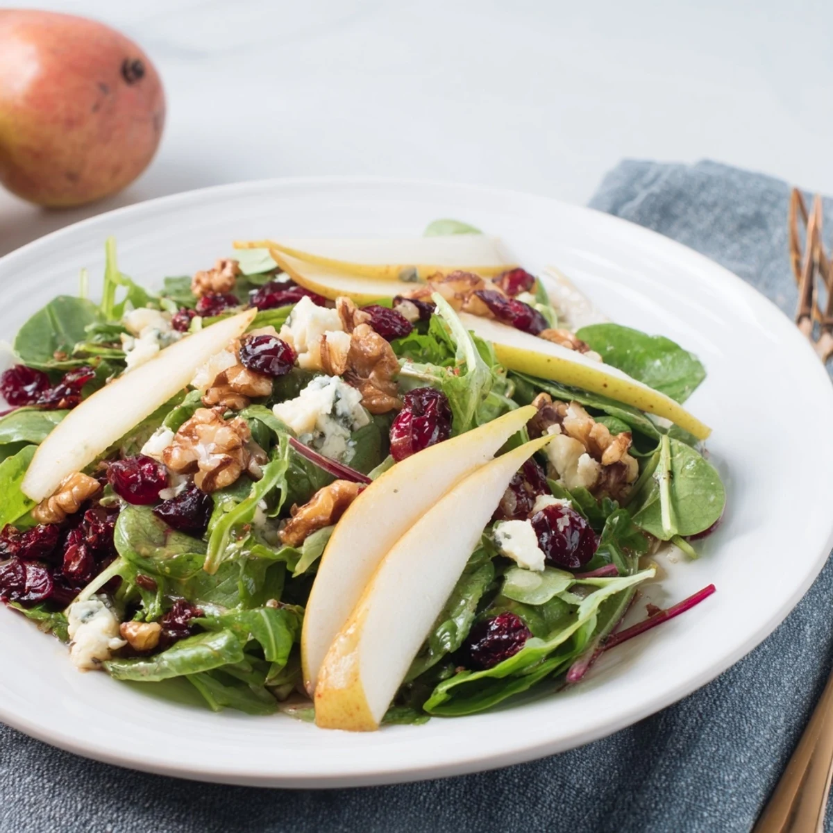 A serving bowl of colorful Pear Gorgonzola Salad with tender greens, sweet pear slices, and crumbled Gorgonzola on a rustic wooden table.