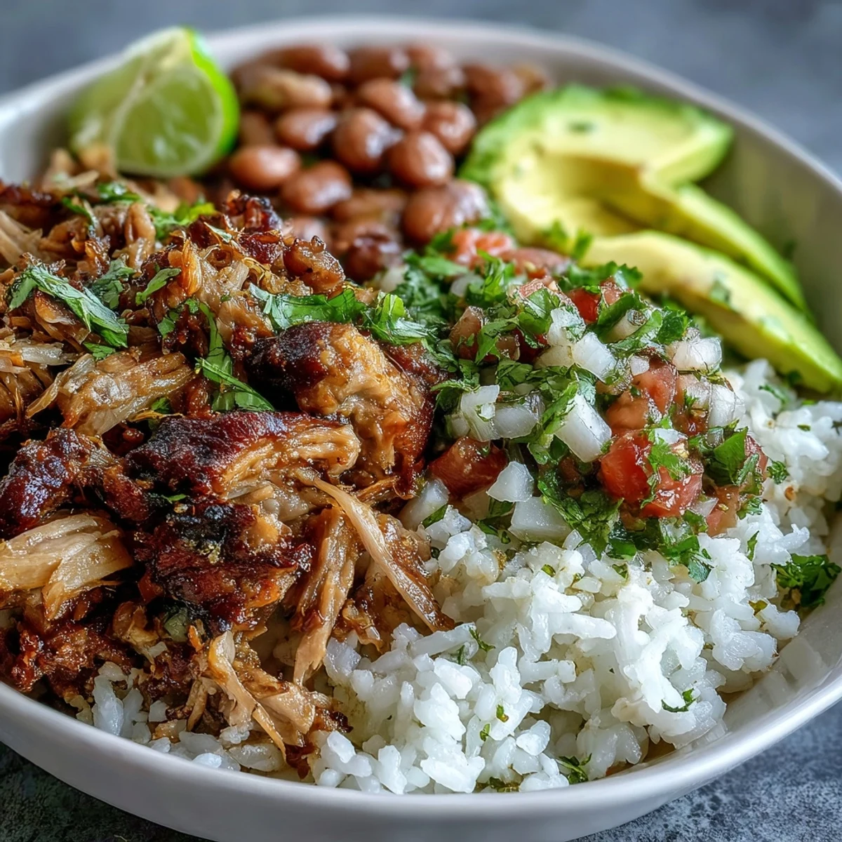 A vibrant Carnitas Bowl featuring slow-cooked shredded pork, fluffy white rice, and hearty pinto beans topped with fresh pico de gallo.