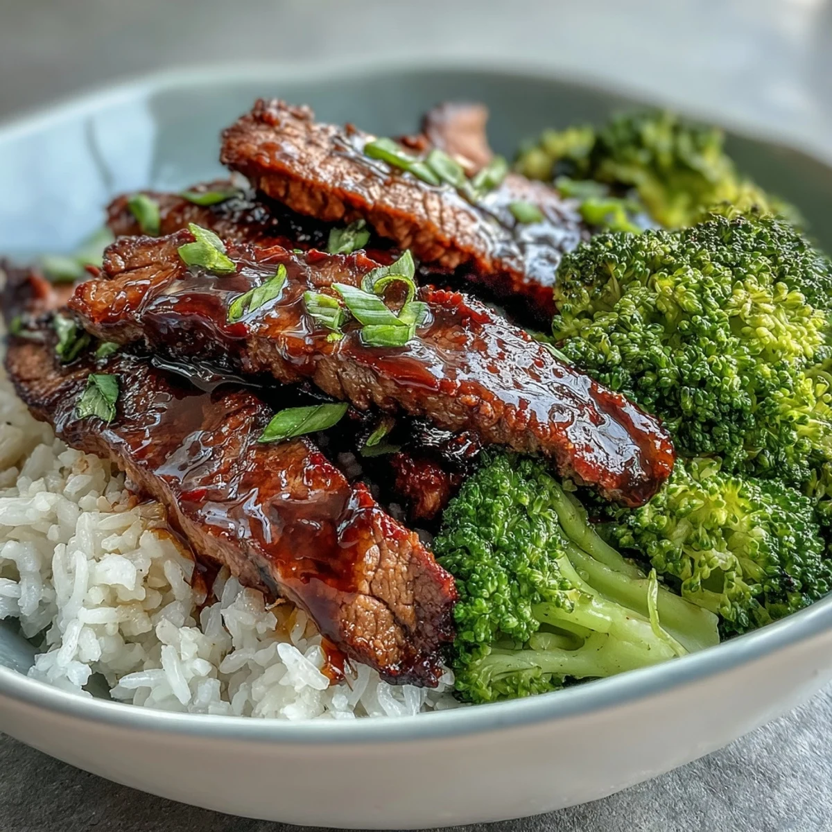 Vivid close-up of tender beef and crisp steamed broccoli over jasmine rice, showcasing the savory sauce pooling around the grains in a Beef and Broccoli Bowl.