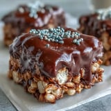 Homemade Chocolate Covered Rice Krispy Treats stacked on a plate, showcasing the crispy cereal texture and gooey marshmallow layer beneath melted chocolate.