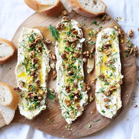 A close-up of Flavored Butter Board Charcuterie spread on a wooden board, topped with chopped nuts, fresh herbs, honey, and flaky salt.