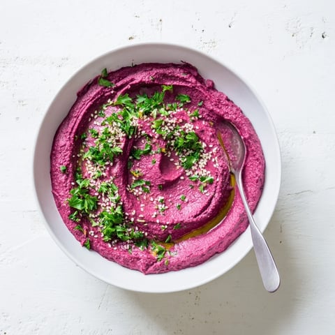 A vibrant pink bowl of homemade Roasted Beet Hummus, garnished with olive oil and fresh parsley, ready for dipping.