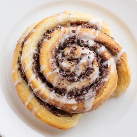Warm Nutella Chocolate Chip Rolls with gooey chocolate swirls are served beside a steaming mug of coffee for a cozy breakfast treat.