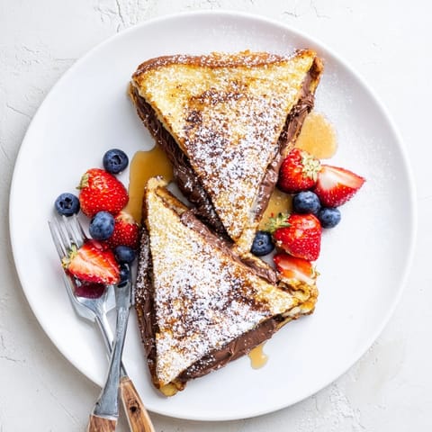 A close-up of two thick Nutella Brioche French Toast slices, revealing a melted chocolate hazelnut filling on a rustic plate.