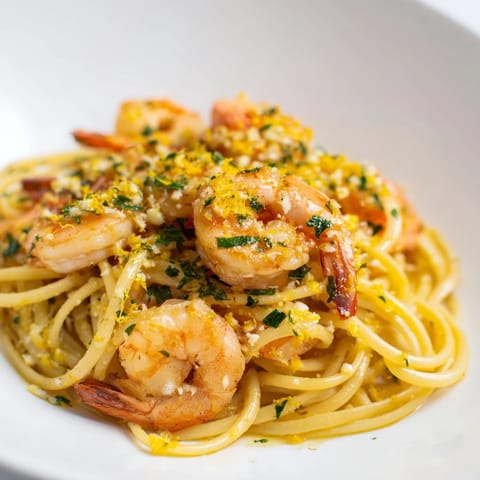 The finished Garlic Butter Shrimp Linguine is served in a white bowl, garnished with lemon zest and grated Parmesan cheese.