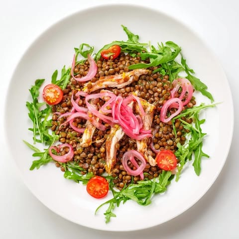 A vibrant serving of Lentil & Chicken Spring Salad with hearty lentils and juicy chicken atop fresh arugula, tangy pickled onions, and a glistening mustard vinaigrette.  