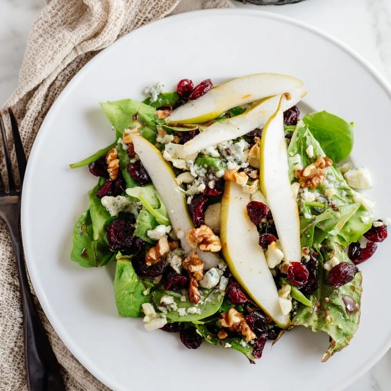 Overhead view of a fresh Pear Gorgonzola Salad topped with toasted walnuts, dried cranberries, and a drizzle of honey-balsamic vinaigrette. 