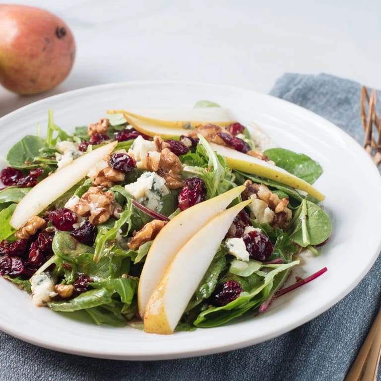 A serving bowl of colorful Pear Gorgonzola Salad with tender greens, sweet pear slices, and crumbled Gorgonzola on a rustic wooden table.