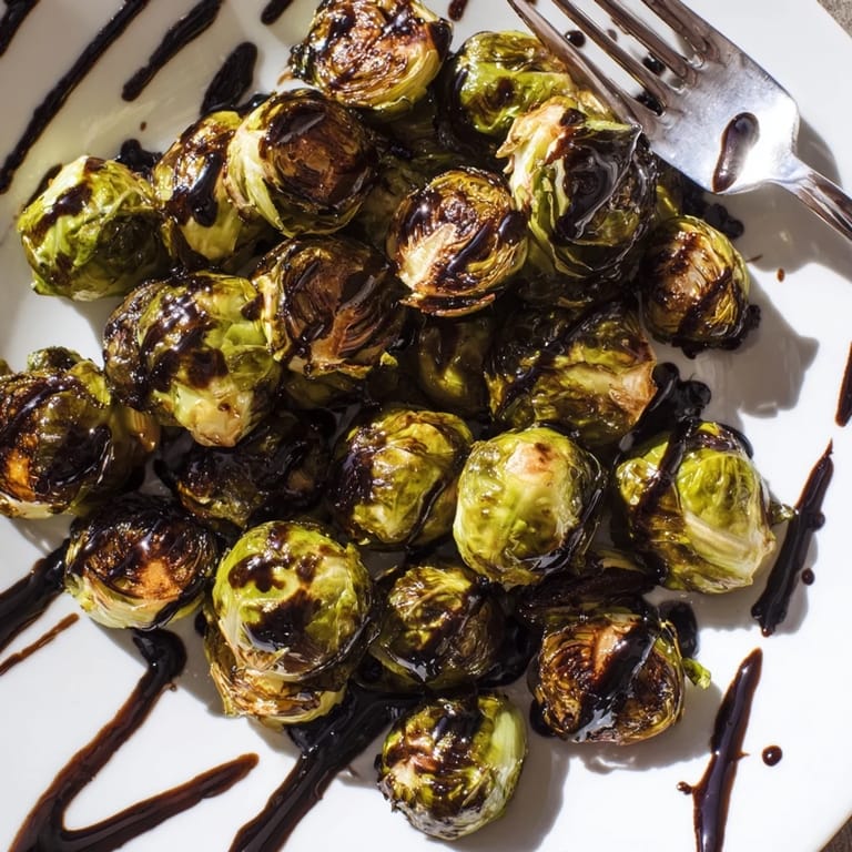 A close-up of glazed Brussels sprouts roasting on a sheet pan with balsamic drizzle for a savory-sweet side dish.