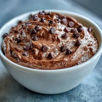 A creamy chocolate cottage cheese brownie batter dip served with fresh strawberries, apple, banana, and grape slices for a protein-packed dessert.